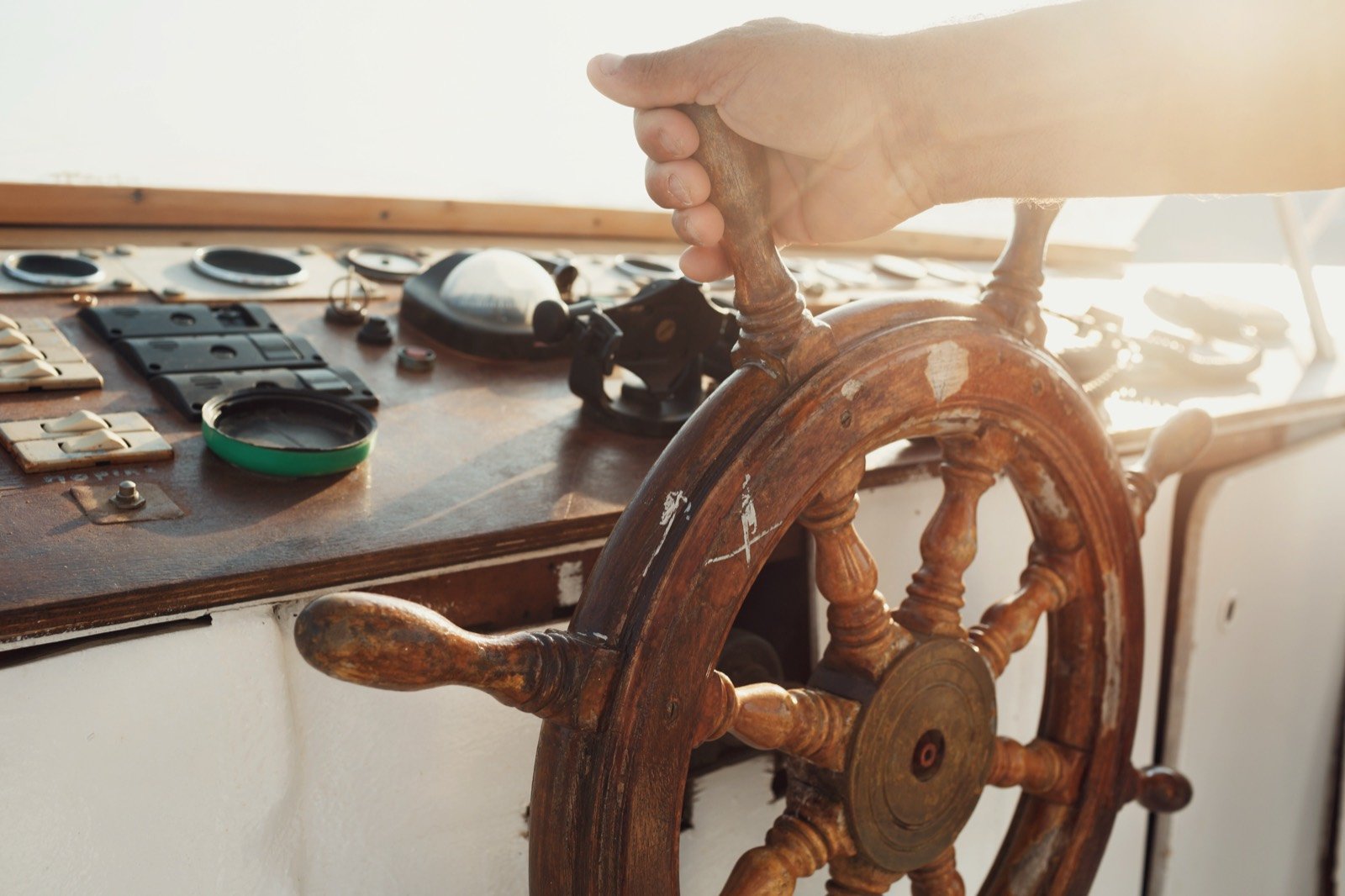 Hand on the wooden helm of a sailboat in warm light